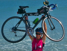 Lynn West Salvo ’71 hoists her bike over her head on the beach